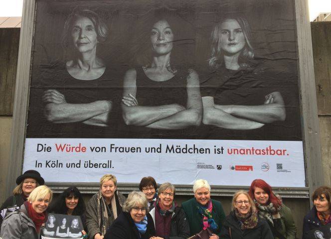 Die Initiatorinnen vor einem der 100 Plakate, die zur Zeit im gesamten Kölner Stadtgebiet hängen.
